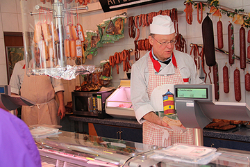 der Ministerpräsident im Ladengeschäft hinter der Theke beim Abwiegen von Aufschnitt