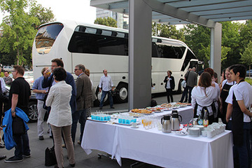 Medienvertreter warten bei einem kleinen Imbiss, vorbereitet durch die Schülerfirma der IGS Mühlenberg; im Hintergrund der Reisebus.