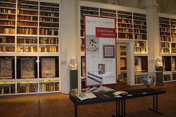 Vitrine mit Ausstellungsstücken vor einer raumhohen Bücherwand