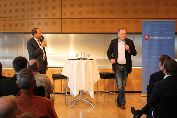 Ministerpräsident Weil und Moderator stehen vor den Besucherinnen und Besuchern