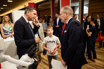 Ministerpräsident Olaf Lies spricht mit dem Hals-Nasen-Ohrenarzt Prof. Thomas Lenarz, zwischen ihnen steht ein Junge, der ein Cochlea-Implantat trägt. Im Hintergrund sich verschiedene Menschen zu sehen.