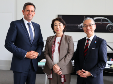 Ministerpräsident Olaf Lies steht mit der japanischen Botschafterin I.E. Mitsuko Shino mit Generalsekretär Sota Toda in seinem Büro. Im Hintergrund ist ein Schreibtisch und ein großformatiges Foto eines VW Käfers zu sehen.