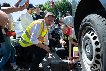 Ministerpräsident Olaf Lies kniet vor einer Apparatur, die das Gewicht eines Wagens kontrolliert. Im Hintergrund sind ein Polizistin und Journalisten zu sehen, die die Szene filmen und fotografieren.