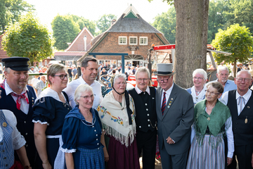 Frauen und Männer in historischen Gewändern stehen mit Ministerpräsident Olaf Lies in einem Halbkreis. Im Hintergrund sind schemenhaft Menschen zu sehen, die auf einem Fest feiern.