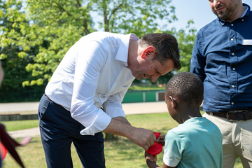 Ministerpräsident Olaf Lies beugt sich zu einem Jungen und hilft ihm bei einem roten Bastelobjekt.