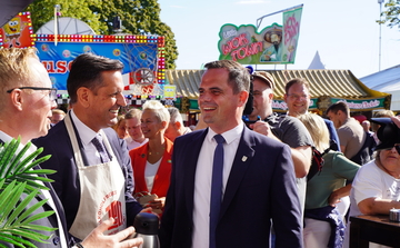 Ministerpräsident Olaf Lies im Gespräch auf dem Stoppelmarkt in Vechta. Im Hintergrund sind Besucherinnen und Besucher des Marktes zu sehen sowie bunte Marktgeschäfte.