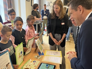 Kinder präsentieren gebastelte Projekte zum plattdeutschen Spracherwerb. Ministerpräsident Lies hört den Erzählungen zu.