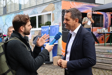 Ministerpräsident Lies steht vor einem Gebäude und gibt einem Reporter ein Interview.