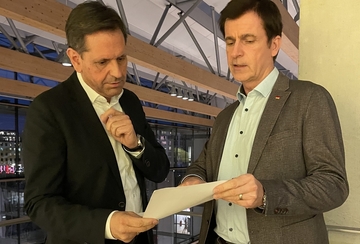 Ministerpräsident Lies steht mit dem Hauptgeschäftsführer des Deutschen Städte- und Gemeindebundes André Berghegger auf einer Empore. Beide blicken auf ein Papier.