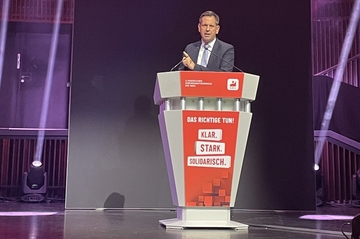 Ministerpräsident Lies steht auf einer Bühne hinter einem roten Rednerpult mit der Aufschrift "Das Richtige tun! Klar. Stark. Solidarisch".