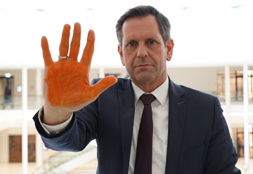 Ministerpräsident Lies zeigt seine Hand mit der orange bemalten Unterseite in die Kamera