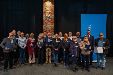 Ministerpräsident Lies steht mit einigen der ausgezeichneten Personen des Tags der Ehrenamtlichen vor dem blauen Banner auf der Bühne