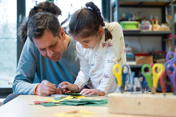 Olaf Lies hilft einem Kind beim Prickeln mit einer Nadel.