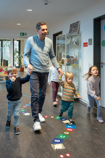 Olaf Lies läuft mit vier Kindern im Flur der Kindertagesstätte, zwei der Kinder halten dabei seine Hand.