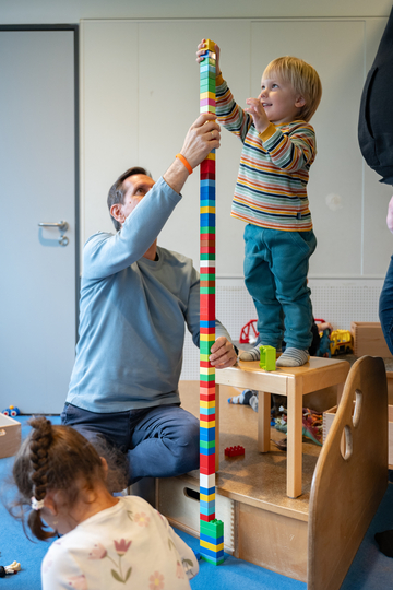 Olaf Lies und ein Kind bauen zusammen einen hohen Turm aus Bausteinen.