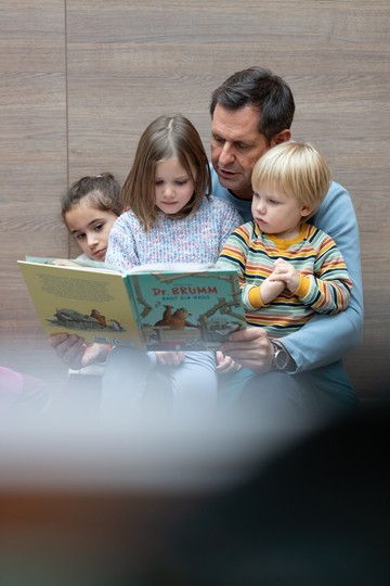 Ministerpräsident Olaf Lies liest drei Kindern ein Buch vor, zwei sitzen auf seinem Schoß.