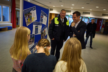 Ministerpräsident Olaf Lies steht mit dem Kontaktbeamten der Polizei Ricklingen vor einer blauen Pinnwand und lässt sich und drei Kindern etwas erklären