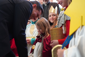 Ministerpräsident Olaf Lies beugt sich zu einem Sternsinger-Mädchen herunter um Geld in ihre Spardose zu tun