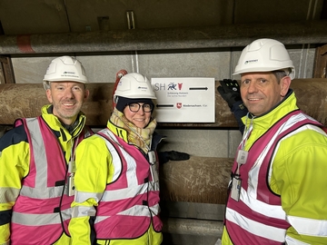 Ministerpräsident Olaf Lies steht vor zwei Rohren und einem Schild, auf dem ein Pfeil nach Schleswig-Holstein und ein Pfeil Richtung Niedersachsen zeigt