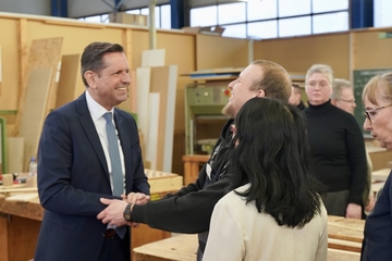 Ministerpräsident Olaf Lies steht in einer Holzwerkstatt und spricht mit einem Mann und einer Frau. Der Mann reicht dem Ministerpräsidenten die Hand, beide lachen. Die Frau steht mit dem Rücken zur Kamera