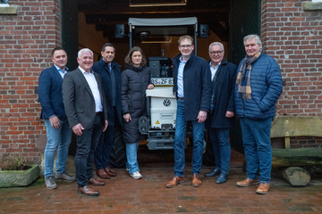 Ministerpräsident Olaf Lies steht mit Vertretern des Hofs Fleming vor einem offenen Tor, im Hintergrund steht ein kleiner Traktor