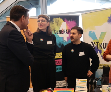 Ministerpräsident Olaf Lies steht an einem Messestand und spricht mit zwei Vertretern