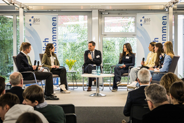 Ministerpräsident Olaf Lies sitzt mit Schülerinnen und Schülern auf einer Bühne, alle halten Mikrofone in der Hand