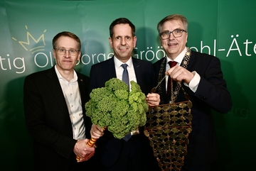 Der Oldenburger Bürgermeister überreicht Ministerpräsident Lies die Grünkohlkönigskette. Der vorherige Grünkohlkönig Daniel Günther hält die Grünkohlpalme
