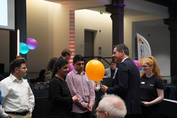 Ministerpräsident Olaf Lies überrreicht einem Jungen einen orangen Luftballon. Andere Kinder stehen drumherum
