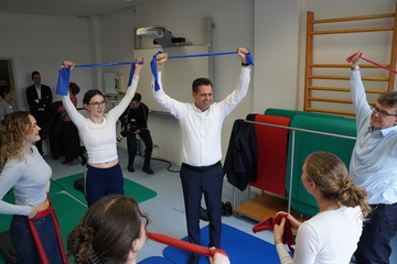 Ministerpräsident Olaf Lies steht mit vier Frauen und einem Mann in einem Kreis und alle versuchen Spannbänder über ihrem Kopf zu halten. Sie sind in einem Sportraum