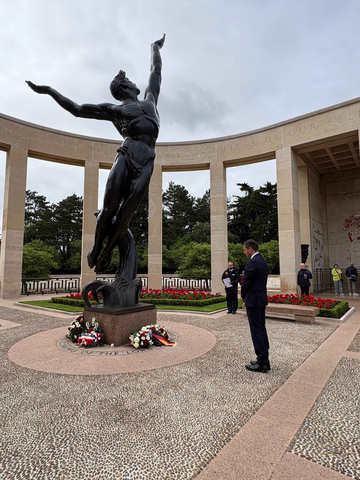 Der niedersächsisches Ministerpräsident Olaf Lies steht auf dem amerikanischen Soldatenfriedhof in Colleville-sur-Me vor einer großen Bronze-Statue vor der mehrere Kränze mit Schleifen niedergelegt sind. Die Szene wird von einem halbkreisförmigen S
