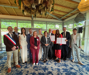 Gruppenfoto einer Delegation aus Niedersachsen und der Normandie in einem lichtdurchfluteten Raum mit großen Fenstern und Holzbalkendecke. Die Teilnehmenden stehen nebeneinander, zwei Personen halten aufgeschlagene Dokumente in den Händen.