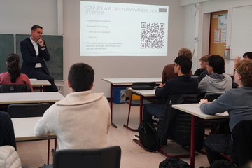 Ministerpräsident Olaf Lies steht in einem Klassenraum vor einer Klasse. An der Wand ist ein QR-Code projieziert