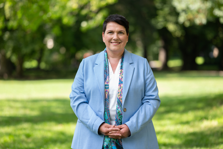 Europaministerin Melanie Walter steht auf einer grünen Wiese im Hintergrund zeichnen sich verschwommen Bäume ab.