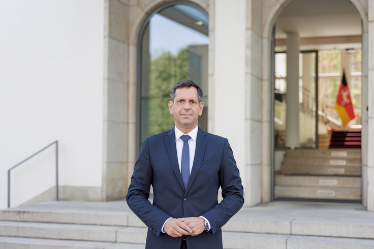 Ministerpräsident Olaf Lies steht vor der Staatskanzlei. Im Hintergrund sind Stufen und die Niedersachsenflagge zu sehen.