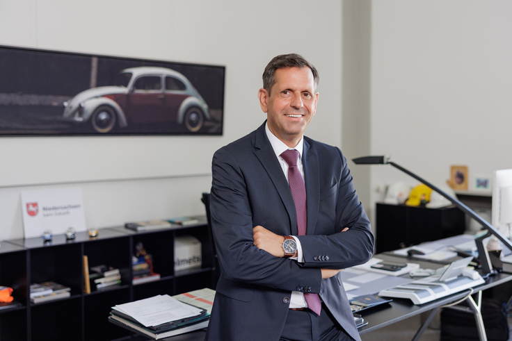 Ministerpräsident Olaf Lies steht angelehnt an seinen Schreibtisch. Im Hintergrund hängt ein Foto eines alten VW Käfer.