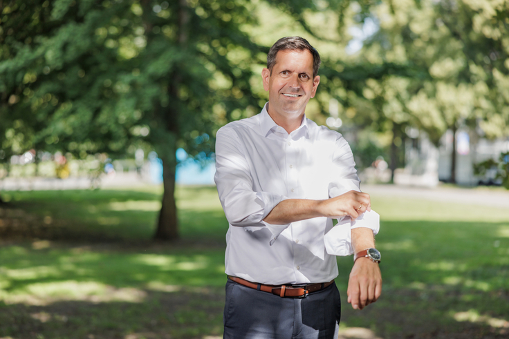 Ministerpräsident Olaf Lies steht im Grünen und krempelt sich den linken Ärmel seines weißen Hemdes hoch. Dabei lächelt er in die Kamera.