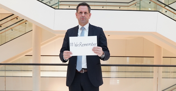 Ministerpräsident Lies hält ein Schild in den Händen mit der Aufschrift: #WeRemember.