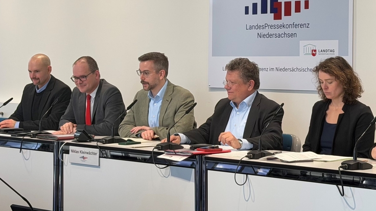 Vier Männer und eine Frau sitzen in einer Reihe und blicken in in den Raum. Im Hintergrund hängt ein Schild an der Wand mit der Aufschrift LandesPressekonferenz Niedersachsen.