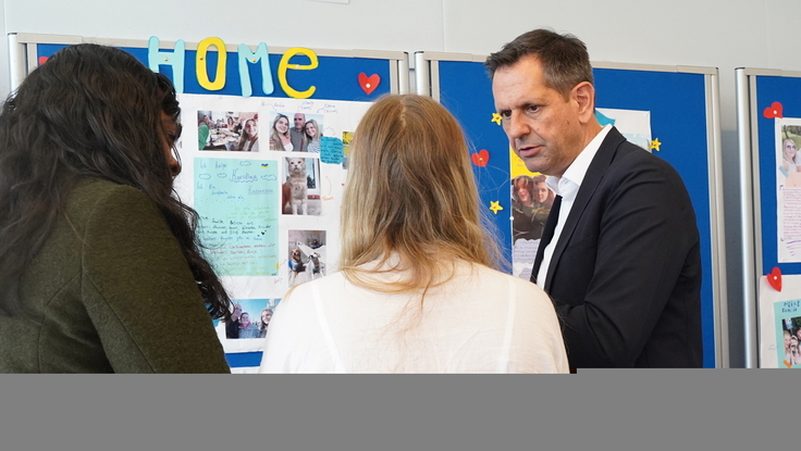 Ministerpräsident Olaf Lies steht mit einer Schülerin und einer Betreuerin vor einer Wandzeitung, auf der Bilder und Texte über die Ukraine gepinnt sind.