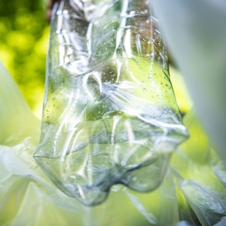 Eine zerdrückte Plastikflasche in einem Plastikbeutel vor grünem Hintergrund.