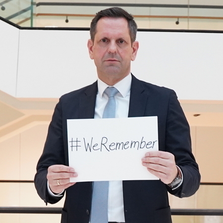 Ministerpräsident Lies hält ein Schild in den Händen mit der Aufschrift: #WeRemember.