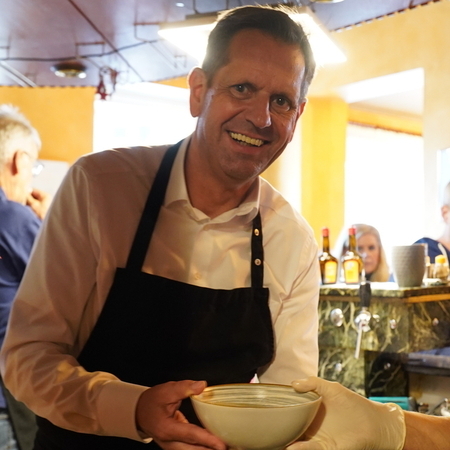 Ministerpräsident Lies überreicht eine Suppenschale an eine Mitarbeiterin einer Suppenküche.