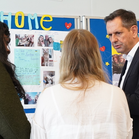 Ministerpräsident Olaf Lies steht mit einer Schülerin und einer Betreuerin vor einer Wandzeitung, auf der Bilder und Texte über die Ukraine gepinnt sind.